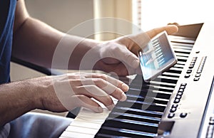 Man watching piano tutorial video with mobile phone. Person practising playing with an online lesson and course.
