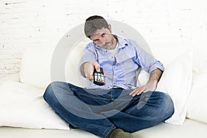 Man watching television at home living room sofa with remote control looking very interested