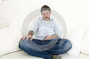 Man watching television at home living room sofa with remote control looking very interested