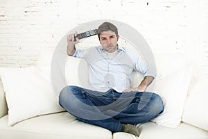 Man watching television at home living room sofa with remote control looking very interested