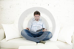 Man watching television at home living room sofa with remote control looking very interested