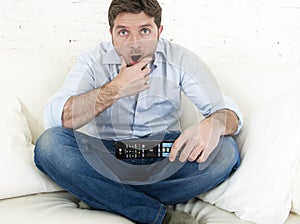 Man watching television at home living room sofa with remote control looking very interested