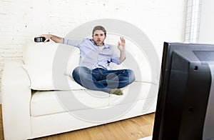 Man watching television at living room sofa with remote control smiling giving okay hand sign