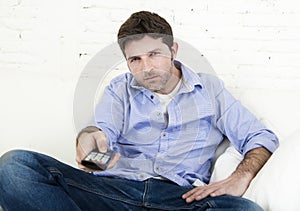 Man watching television lying at home living room sofa with remote control looking very interested