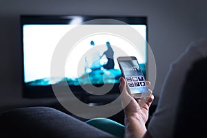 Man watching television and using smart tv remote control app.