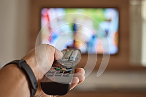 Man watching TV in the room and switches channels using the remote control in his hand