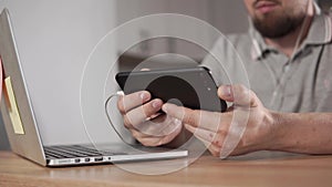 Man is watching video on display of modern smartphone with headphones, close-up