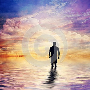 Man in water of calm ocean looking at the fairytale, fantastic sunset sky.