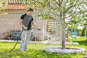 Man watering the fruit trees with a hose on a country site