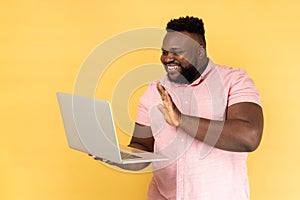 Man waving hand, gesturing hello to laptop screen, video call with friend, communicating online.