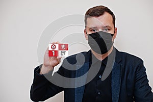 Man wear black formal and protect face mask, hold Leicestershire flag card isolated on white background. United Kingdom counties