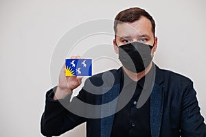 Man wear black formal and protect face mask, hold Merionethshire flag card isolated on white background. United Kingdom counties