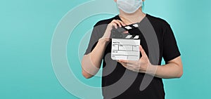 Man wear face mask and hand hold clapper board or movie slate. it use in video production and cinema industry on green or mint