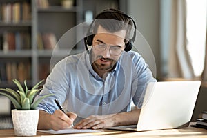 Man wear headphones watch webinar using laptop writing notes