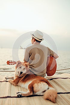 A man wear straw hat and playing guitar music song near the sea sunset with a dog pet..Travel, Vocation, Holiday concept.