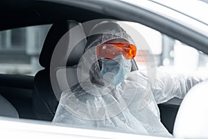 Man Wearing Anti COVID Protective Suit, Glasses, Medicine Mask and Gloves and Driving. Living According to New Epidemia photo