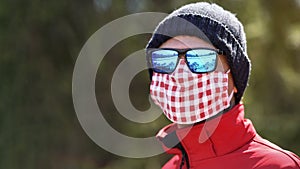 Man wearing beanie hat, blue shiny sunglasses and white red cotton home made nose mouth face virus mask, closeup detail portrait,