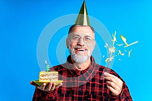 man wearing birthday hat with cake isolated on bright blue colour background, studio portrait