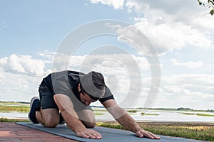 Man wearing a black shirt and dark green shorts laying forward in child`s pose in attempt to correct his bodies posture in front