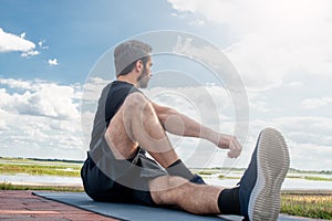 Man wearing a black shirt and dark green shorts laying forward in hip stretching pose in attempt to correct his bodies posture in