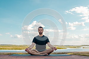 Man wearing a black shirt and dark green shorts sits with legs crossed in lotus pose in attempt to correct his bodies posture in