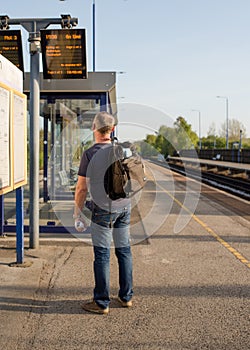 Man wearing black shirt and jeans with green travel backpack / rucksack looking at electronic board and train schedules at the