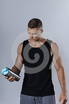 Man wearing blank black tank top is drinking protein or other supplement from a metal shaker