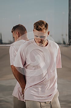 Man wearing blank t-shirt posing against glass mirror wall in the city street, front tshirt mockup on model