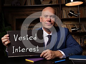 Man wearing blue business suit and showing blank black notepad with written text Vested Interest