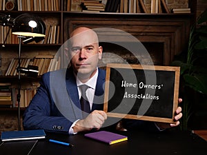 Man wearing blue business suit and showing chalkboard with written text Home Owners` Associations