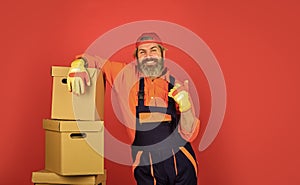 Man wearing boilersuit packing boxes. move to new apartment. bearded loader in uniform. Cardboard boxes. moving to new