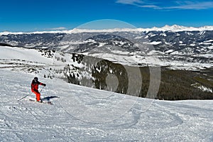 Man wearing bright red suit skiing on snowy backcountry bowl area. Extreme winter sports.