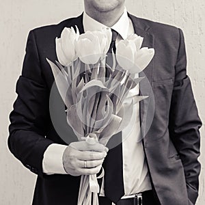 A man wearing a business suit, holding a bouquet of tulips. The man gives a bouquet of flowers.