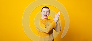 Man wearing casual sweater over yellow background clapping and applauding happy and joyful, smiling proud hands together.