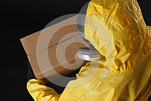 Man wearing chemical protective suit with cardboard box on background, above view. Prevention of virus spread