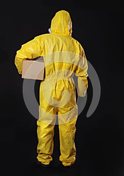 Man wearing chemical protective suit with cardboard box on background, back view. Prevention of virus spread
