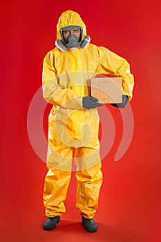 Man wearing chemical protective suit with cardboard box on background. Prevention of virus spread