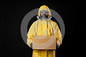 Man wearing chemical protective suit with cardboard box on background. Prevention of virus spread