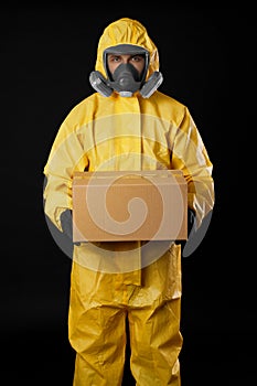 Man wearing chemical protective suit with cardboard box on black background. Prevention of virus spread