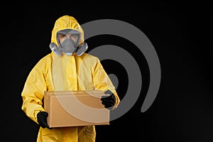 Man wearing chemical protective suit with cardboard box on black background. Prevention of virus spread