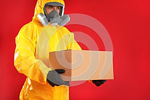 Man wearing chemical protective suit with cardboard box on red background. Prevention of virus spread