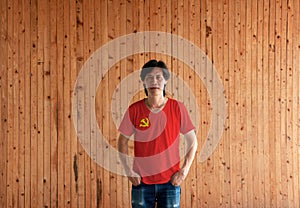 Man wearing Chinese Communist Party flag color shirt and standing with two hands in pant pockets on the wooden wall background