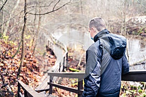 Man wearing a corona virus mask while walking outdoors in the nature in winter or autumn. Young person hiking the forest.