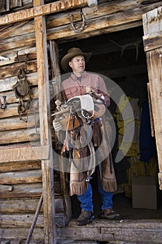 Man Wearing Cowboy Hat Holding a Saddle