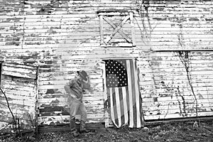 Man wearing cowboy hat standing in front of old abandoned barn with American flag