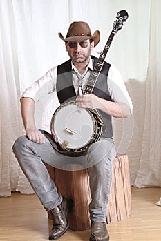Man wearing cowboy leather hat and sunglasses holding banjo