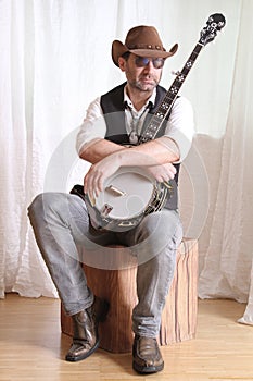 Man wearing cowboy leather hat and sunglasses holding banjo with crossed arms