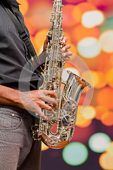 Man wearing dark shirt and jeans playing saxophone, posing from profile angle