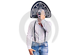 Man wearing day of the dead costume over background covering one eye with hand, confident smile on face and surprise emotion