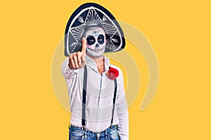 Man wearing day of the dead costume over background pointing with finger up and angry expression, showing no gesture